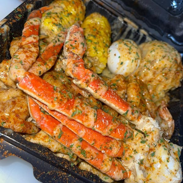 A close-up of Goldie's seafood boil with crab legs, corn, eggs, and shrimp in a black container.