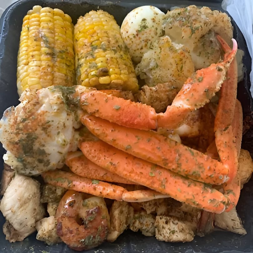 Goldie's Seafood boil with crab legs, corn on the cob, potatoes, and shrimp in a black container.