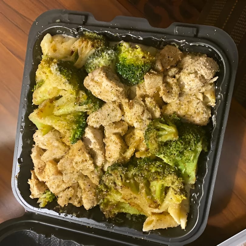 Chicken and broccoli pasta in a black takeout container, with penne pasta visible.