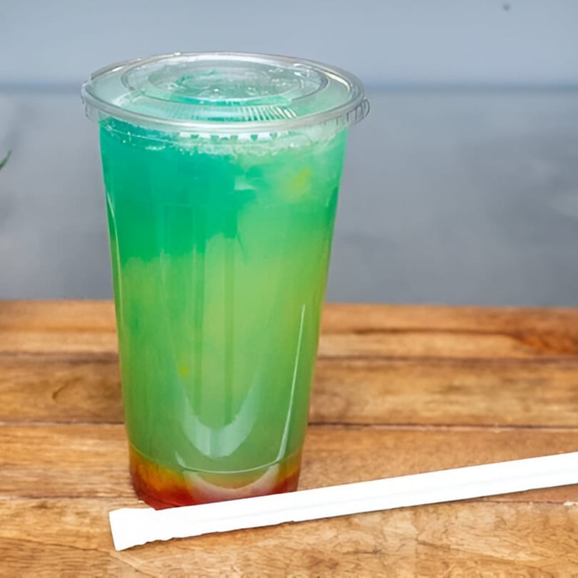 A vibrant blue and green layered drink with red fruit at the bottom, on a wooden table.